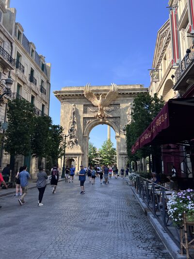 The Ministry of Magic streets at Epic Universe: 1920s Parisian architecture with a golden archway and cobblestone streets